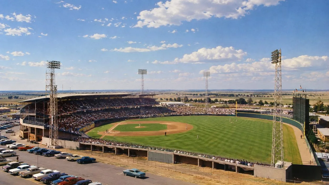 A vintage-style view of an open-air baseball stadium on flat prairie land